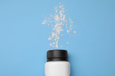 Photo of Bottle and scattered dusting powder on light blue background, top view. Baby cosmetic product
