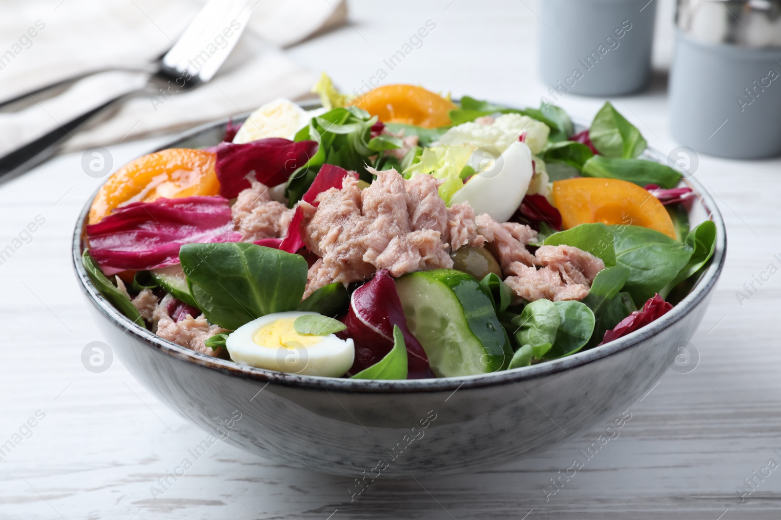 Photo of Bowl of delicious salad with canned tuna and vegetables on white wooden table, closeup