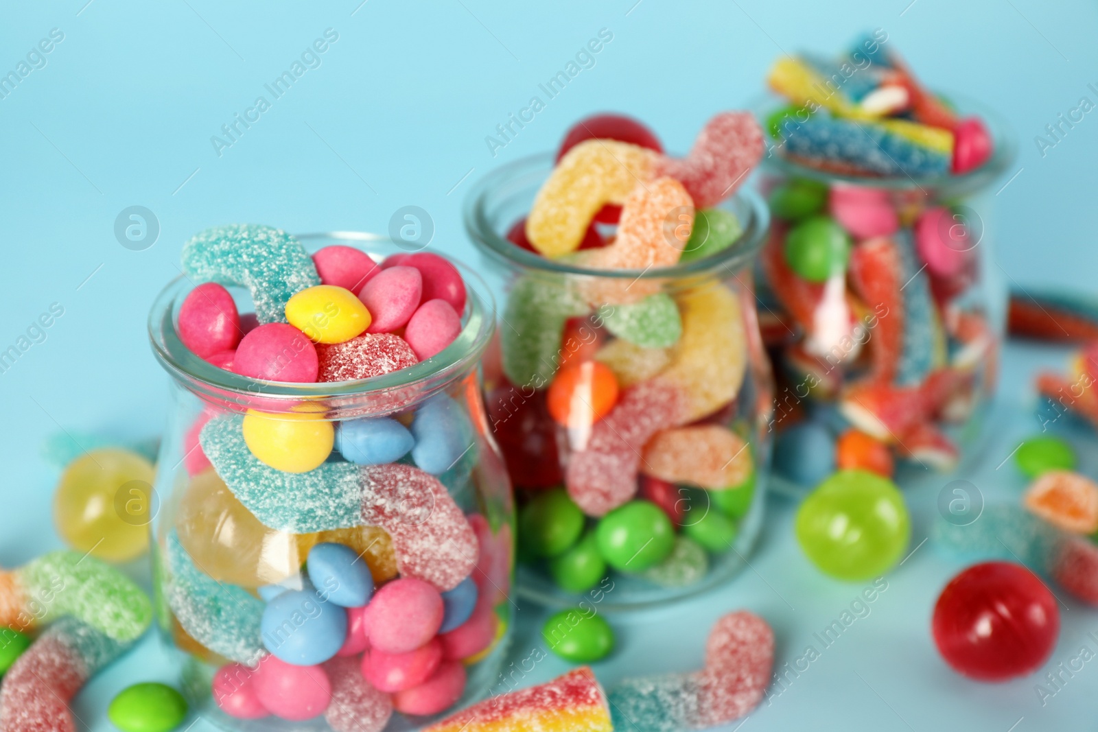 Photo of Jars with different delicious candies on light blue background