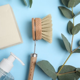 Cleaning supplies for dish washing and eucalyptus branch on light blue background, flat lay