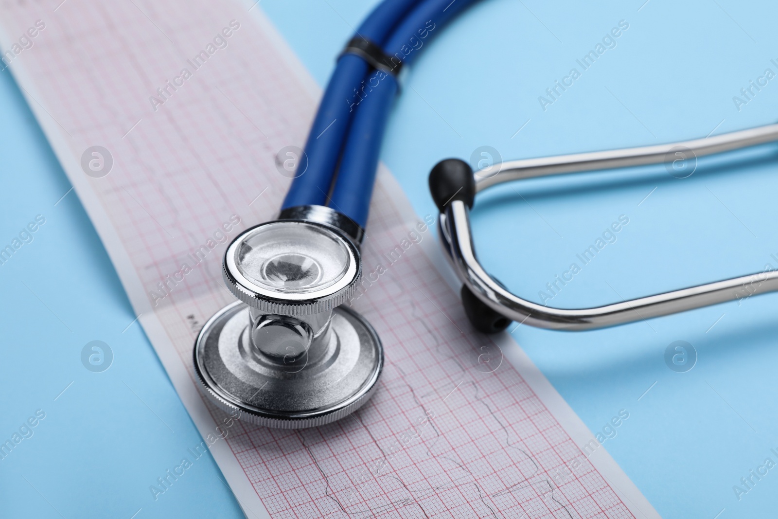 Photo of Stethoscope and cardiogram paper on light blue background, closeup