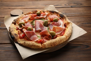 Photo of Tasty pizza with cured ham, olives and sun-dried tomato on wooden table