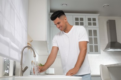 Photo of Man filling glass with water from tap in kitchen