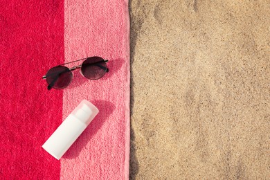 Photo of Beach towel with sunglasses and sunscreen on sand, flat lay. Space for text
