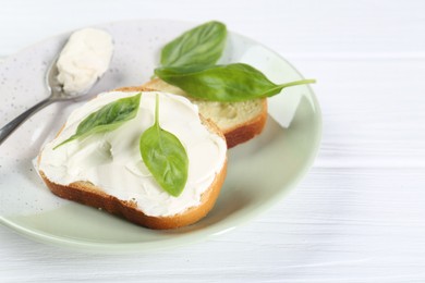 Photo of Pieces of bread with cream cheese and basil leaves on white wooden table. Space for text