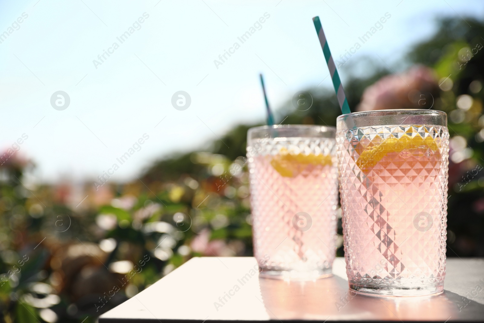 Photo of Glasses of pink rose lemonade on  table in blooming garden. Space for text