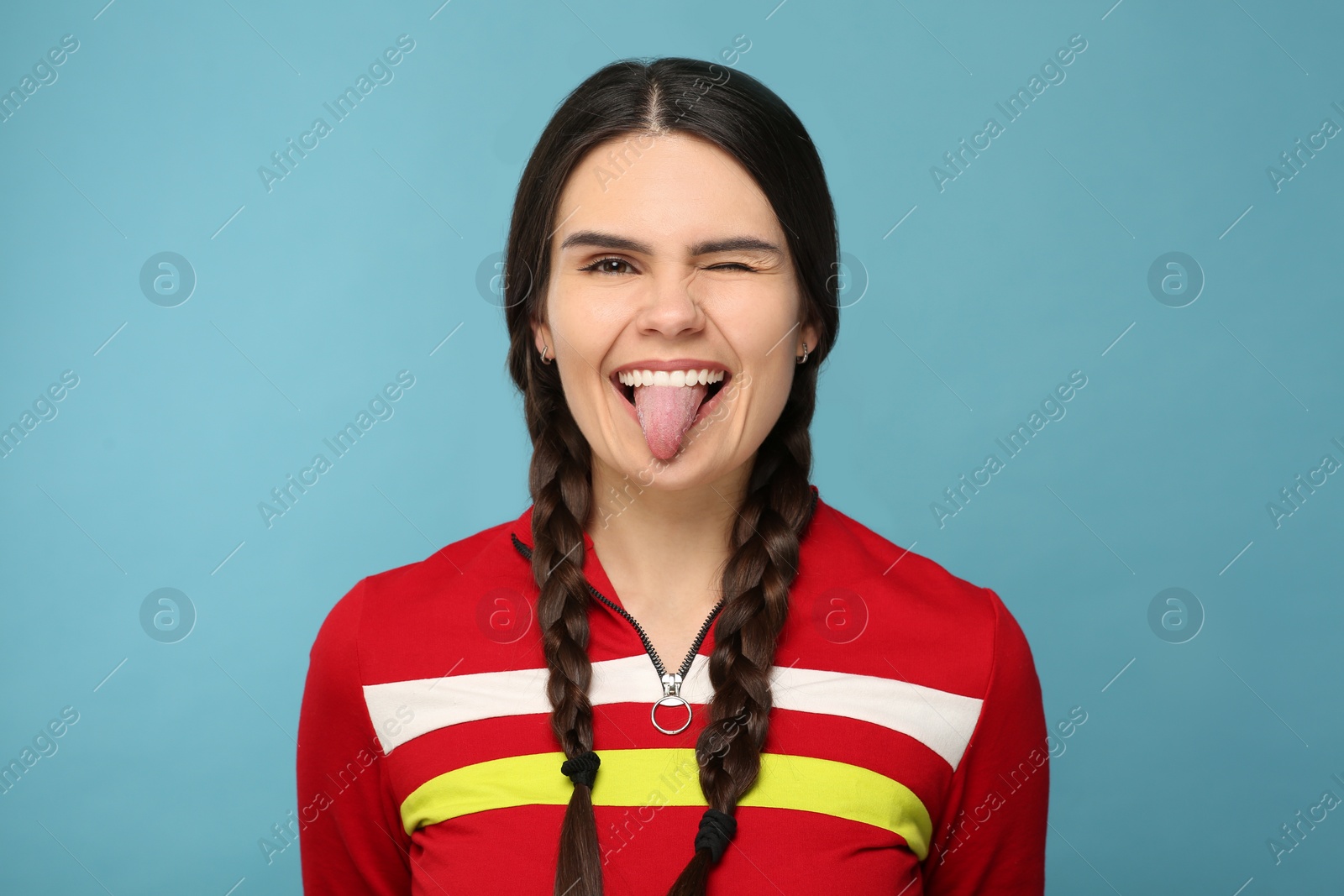 Photo of Happy young woman showing her tongue on light blue background