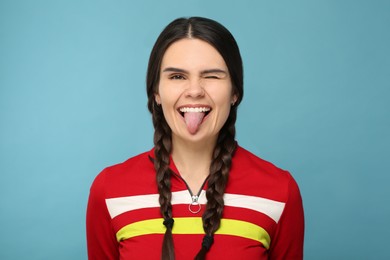 Photo of Happy young woman showing her tongue on light blue background