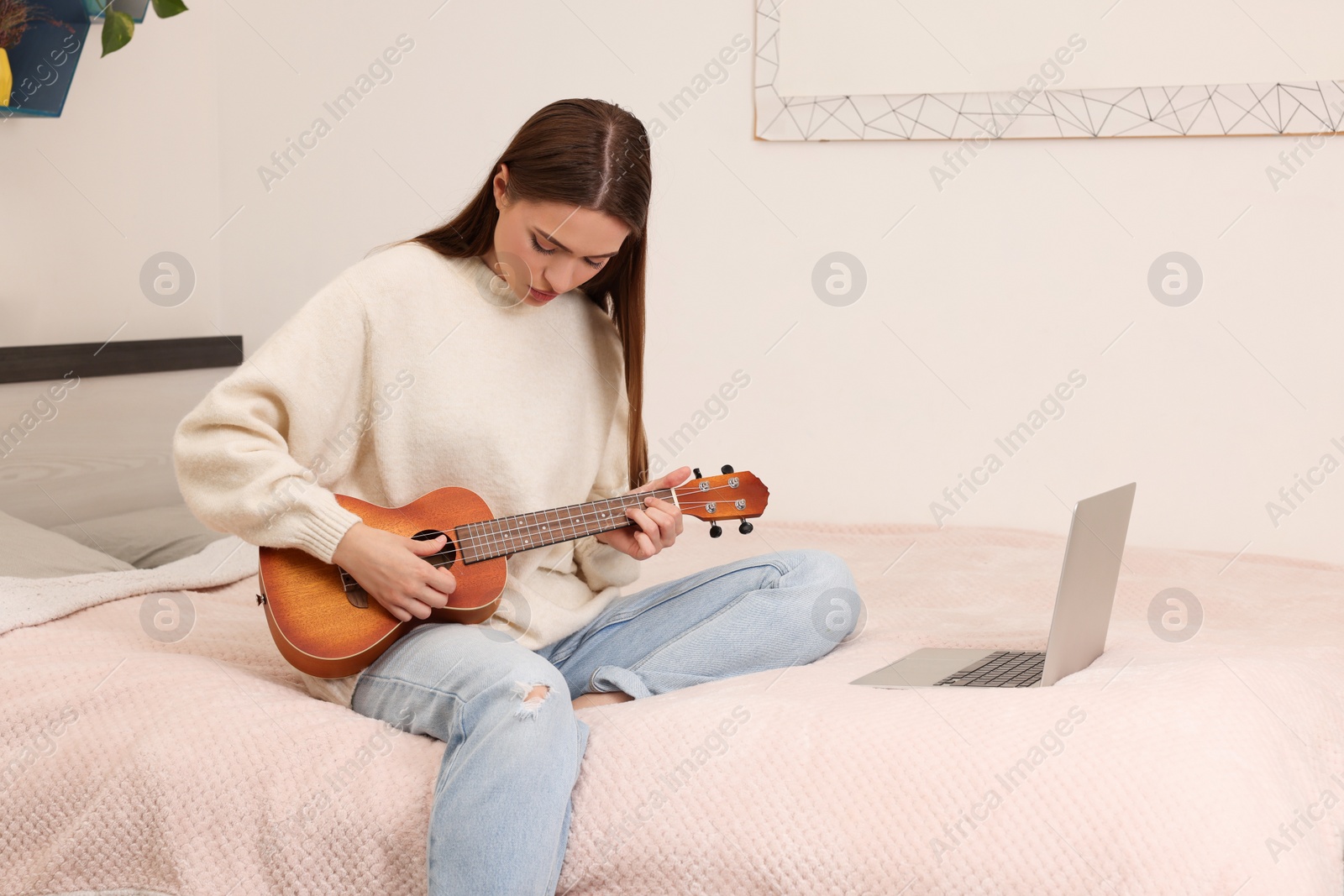 Photo of Happy young woman learning to play ukulele with online music course at home. Time for hobby