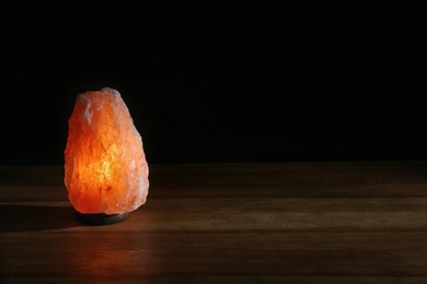 Photo of Himalayan salt lamp on table against black background. Space for text