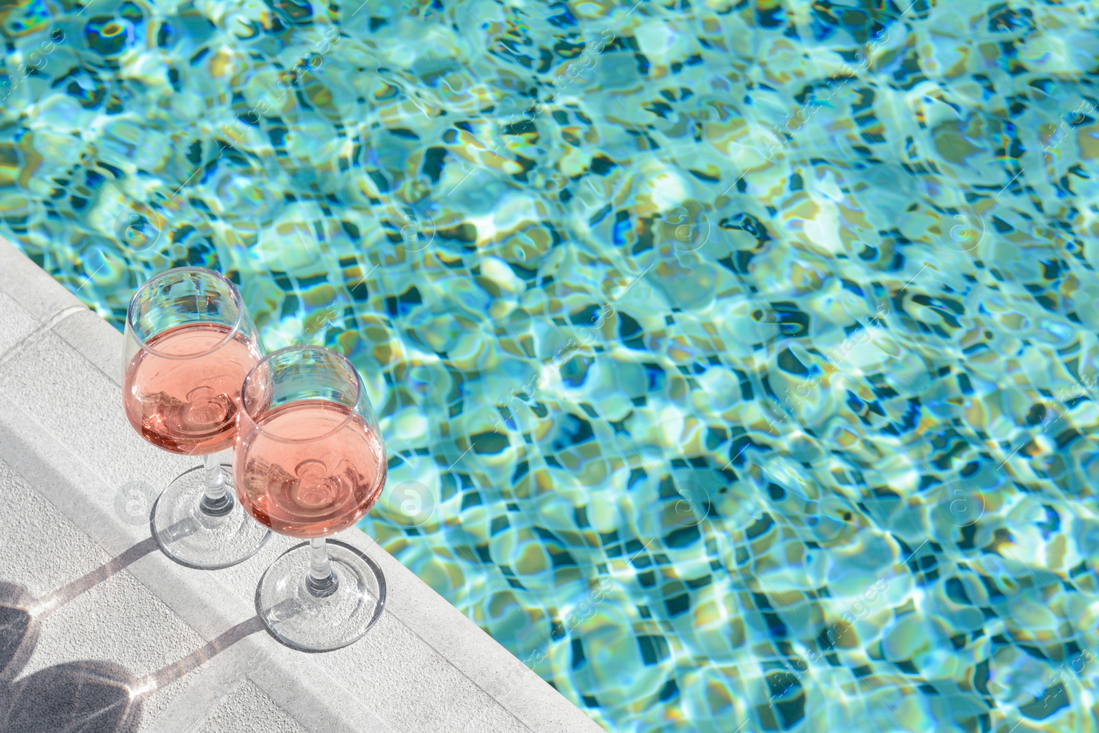 Photo of Glasses of tasty rose wine on swimming pool edge, space for text