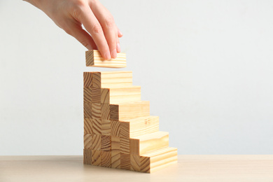 Photo of Woman building steps with wooden blocks at table, closeup. Career promotion concept