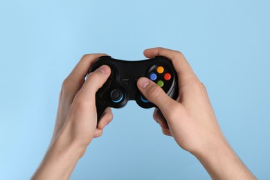 Man using wireless game controller on light blue background, closeup