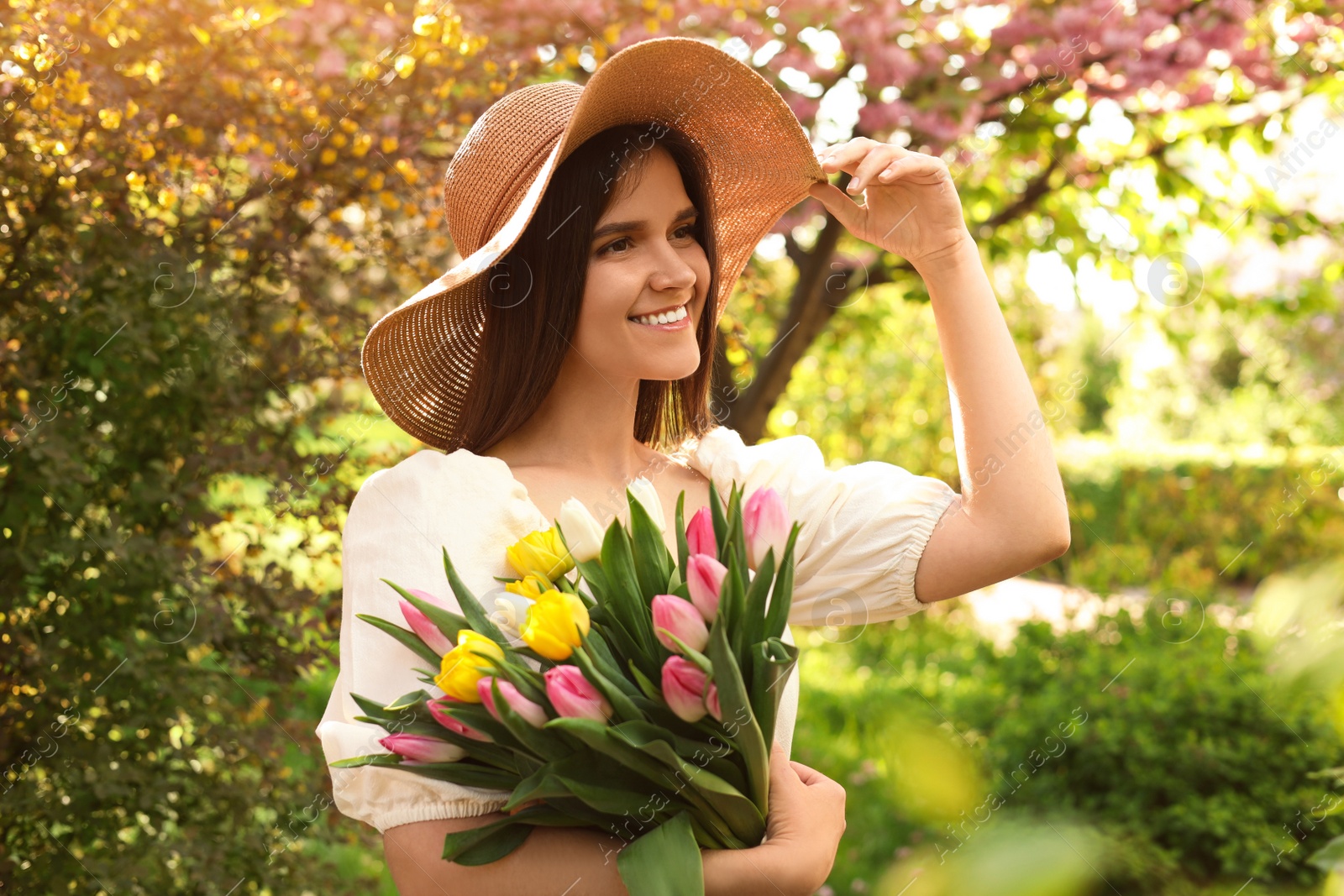 Photo of Beautiful young woman with bouquet of tulips in park on sunny day