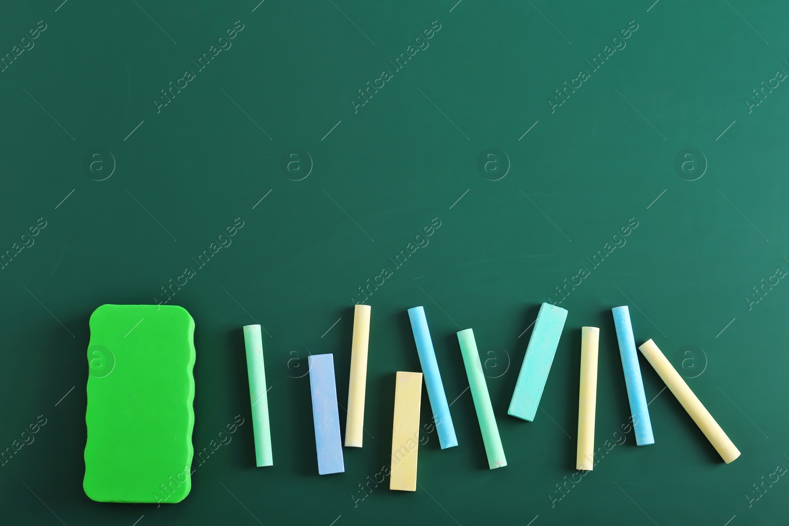Photo of Pieces of chalk and blackboard duster on green background, top view