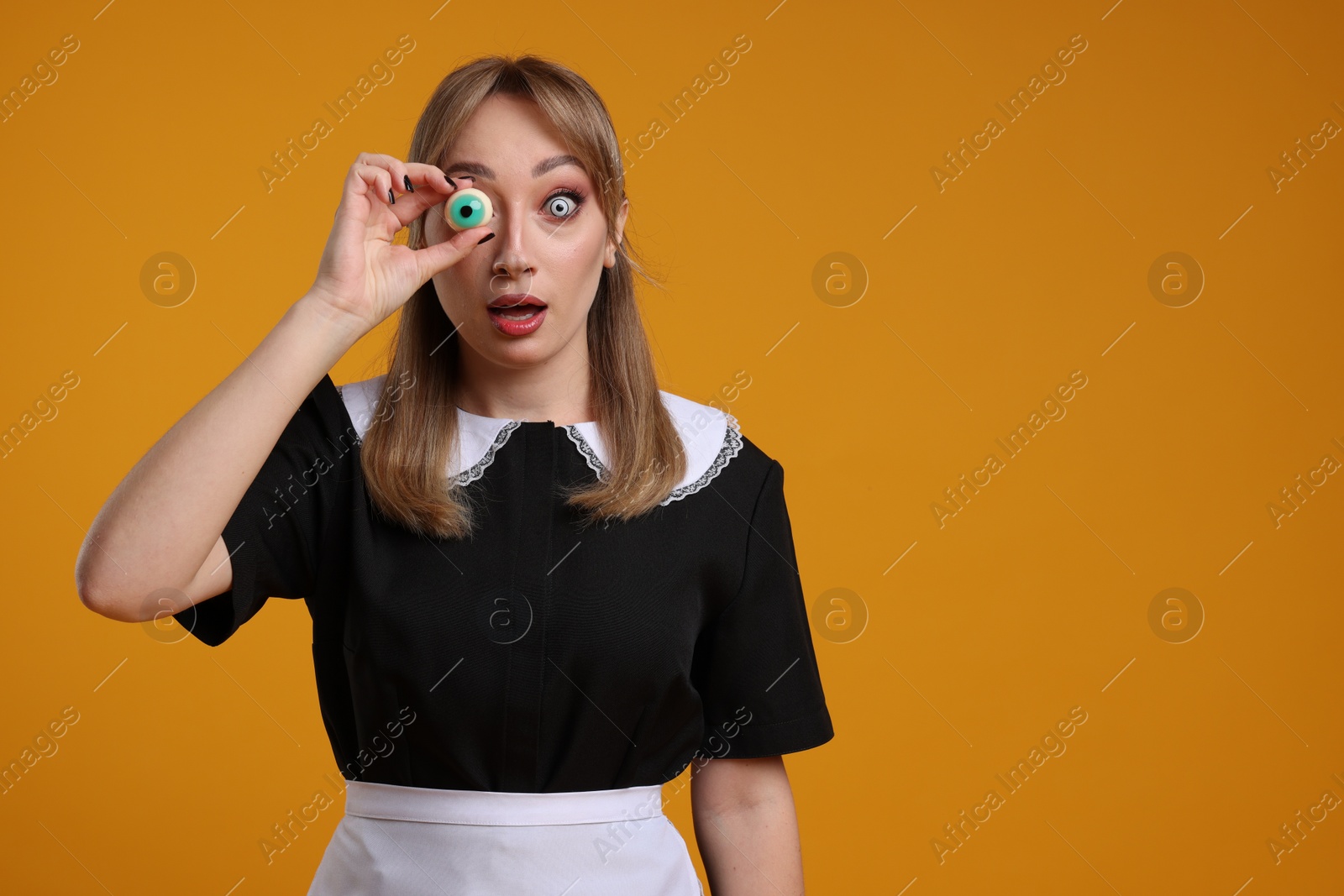 Photo of Emotional woman in scary maid costume with decorative eyeball on orange background, space for text. Halloween celebration