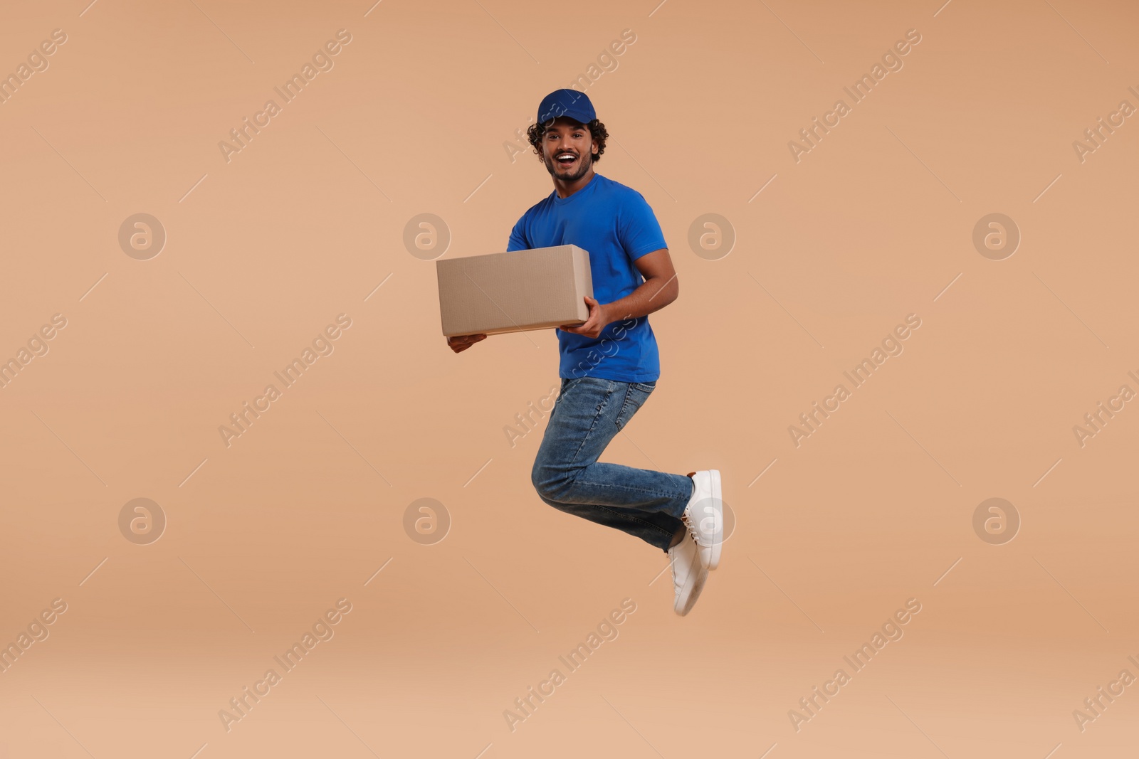 Photo of Happy courier with parcel jumping on light brown background, space for text