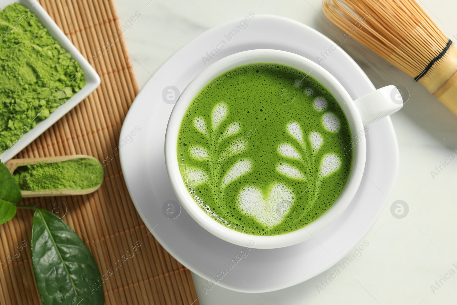 Photo of Delicious matcha latte, powder, leaf and whisk on white table, flat lay