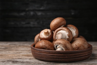 Photo of Bowl of fresh champignon mushrooms on table against black background. Space for text