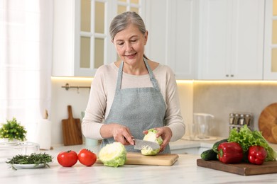 Photo of Happy housewife cutting cabbage at table in kitchen