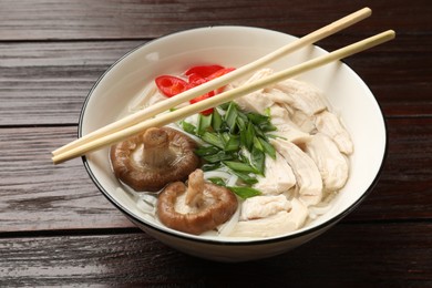 Delicious ramen with meat in bowl and chopsticks on wooden table, closeup. Noodle soup