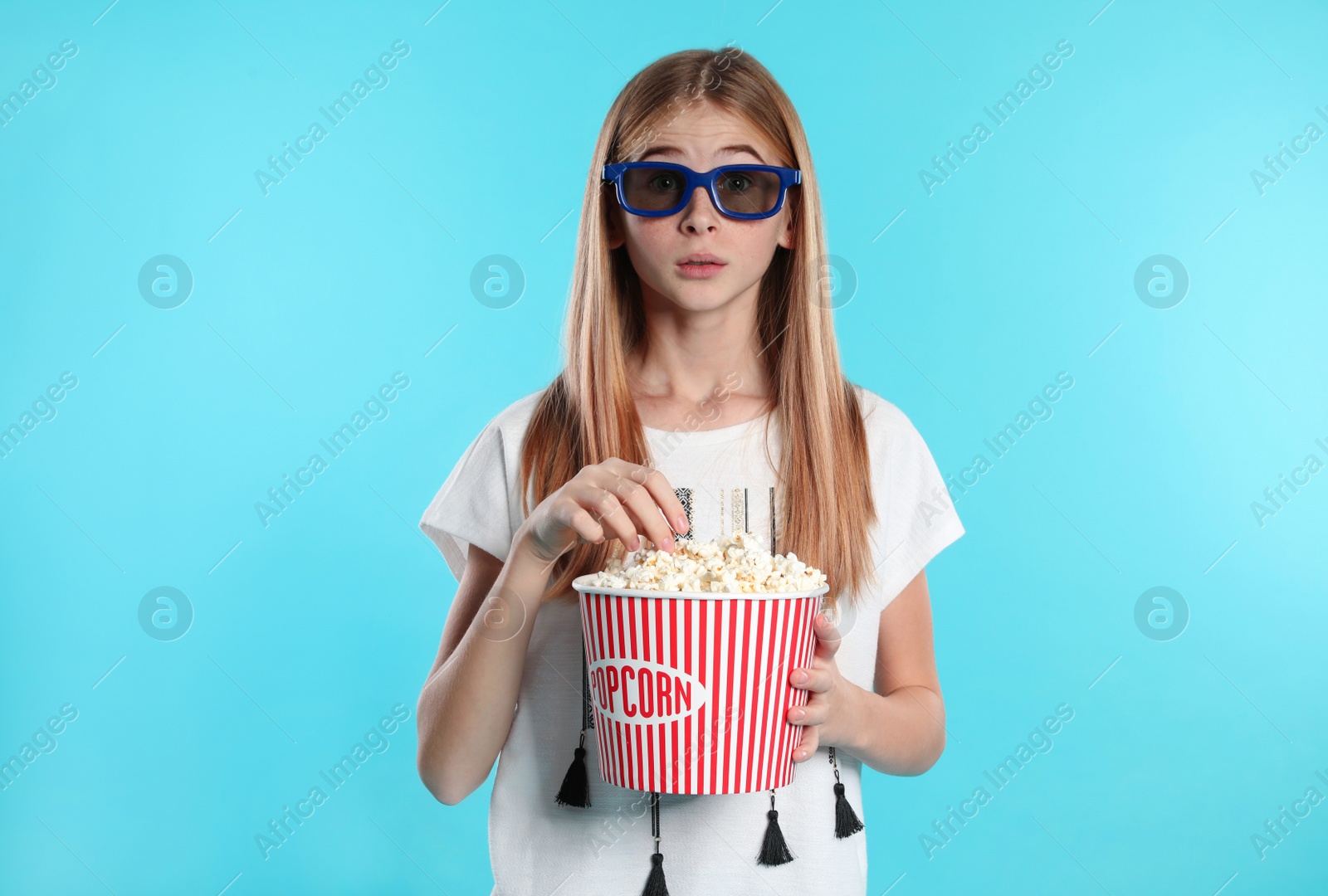 Photo of Emotional teenage girl with 3D glasses and popcorn during cinema show on color background