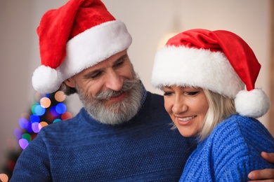 Photo of Happy mature couple in Santa hats celebrating Christmas at home