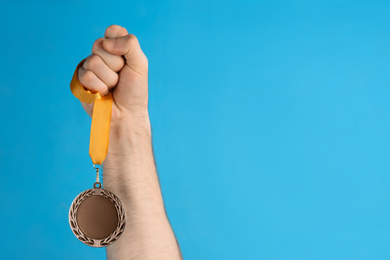 Photo of Man holding golden medal on blue background, closeup. Space for design