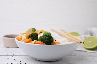 Photo of Bowl of rice with fried tofu, broccoli and carrots on white wooden table, closeup