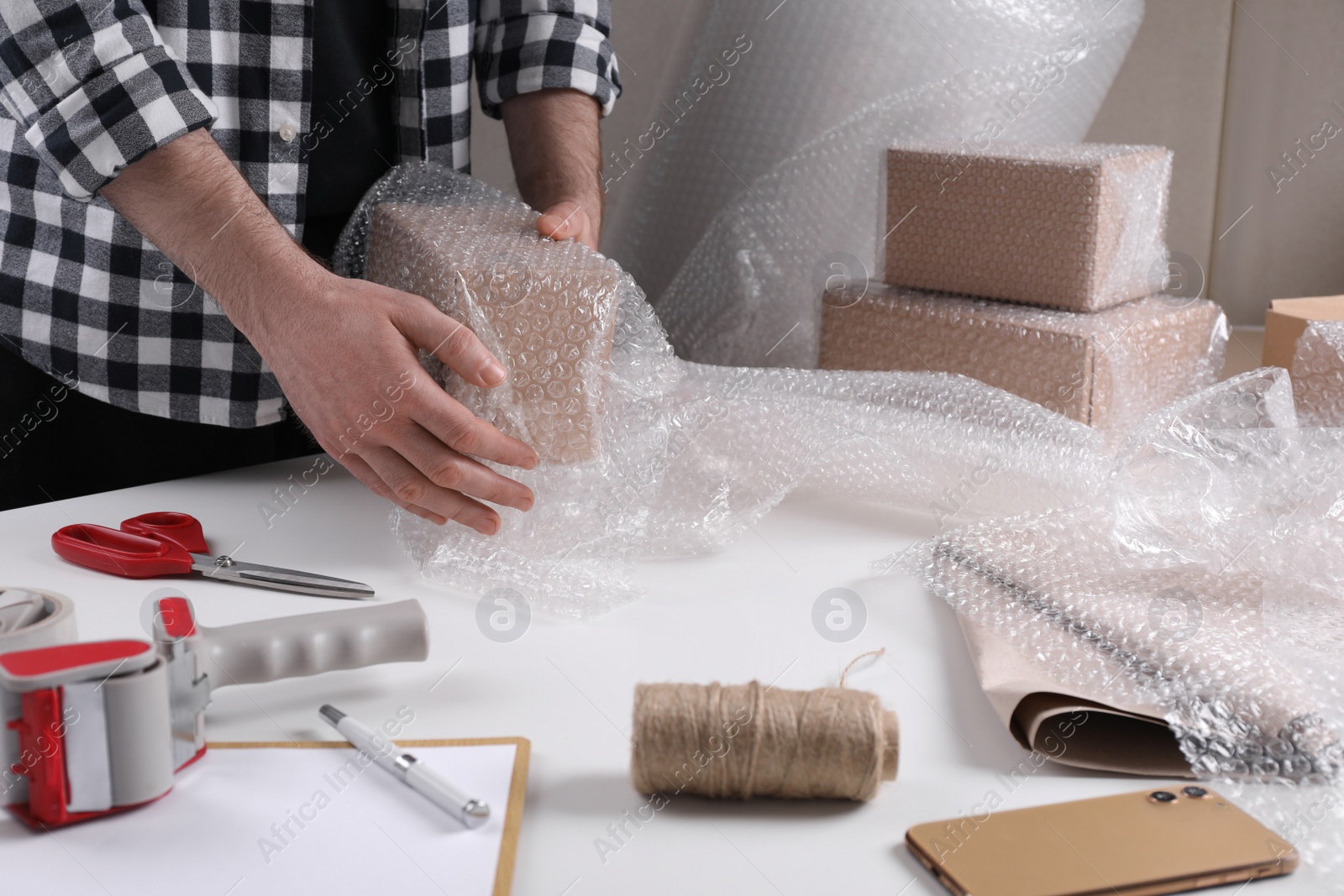 Photo of Man covering box with bubble wrap at table in warehouse, closeup