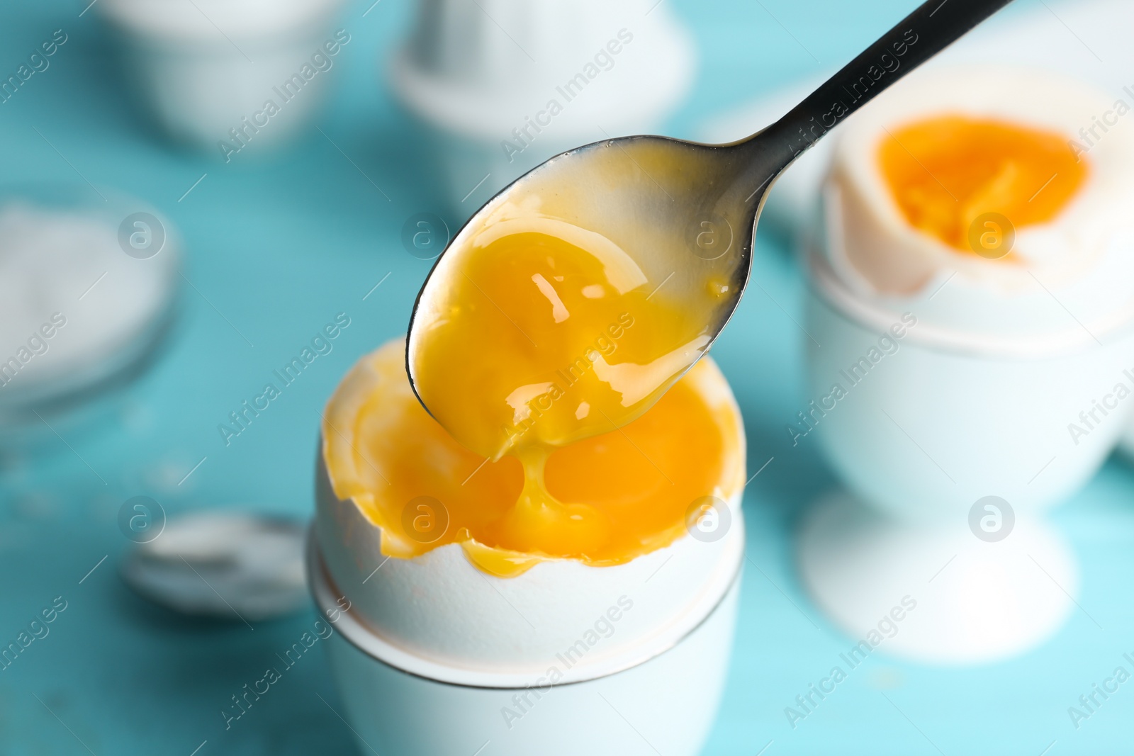 Photo of Eating soft boiled chicken egg with spoon at light blue table, closeup