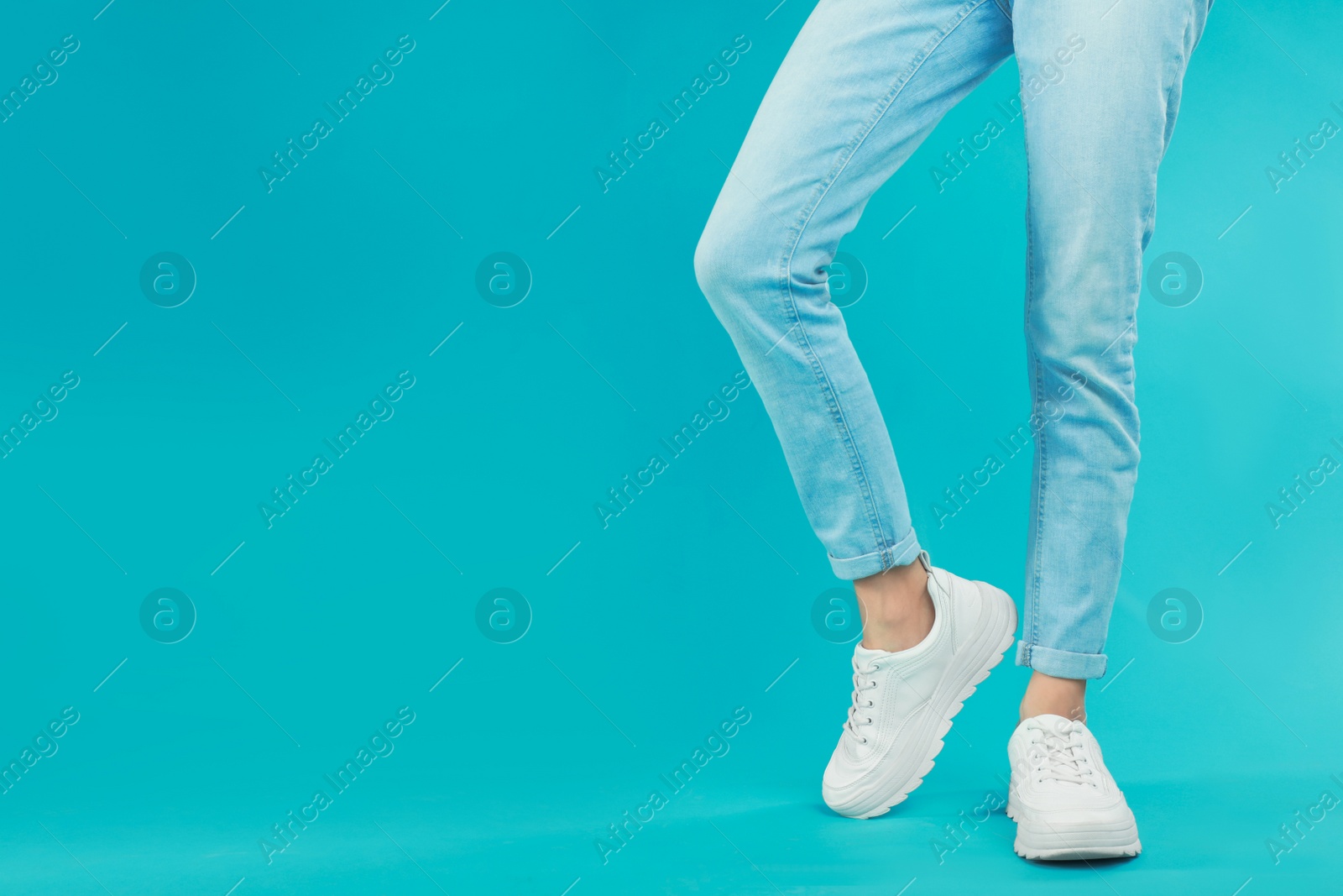 Photo of Woman in stylish sport shoes on light blue background. Space for text