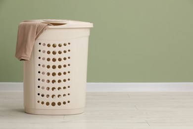 Photo of Plastic laundry basket with clothes near light green wall. Space for text