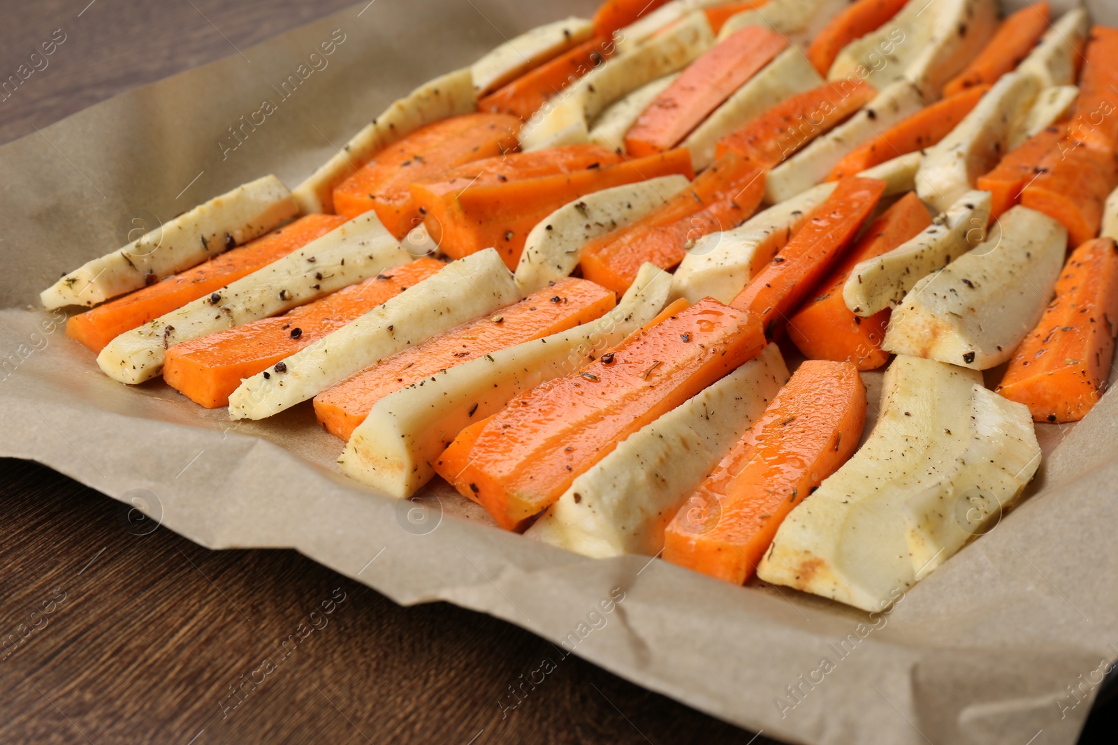 Photo of Baking tray with parchment, parsnips and carrots on wooden table, closeup