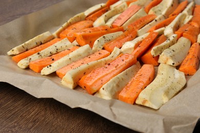 Photo of Baking tray with parchment, parsnips and carrots on wooden table, closeup