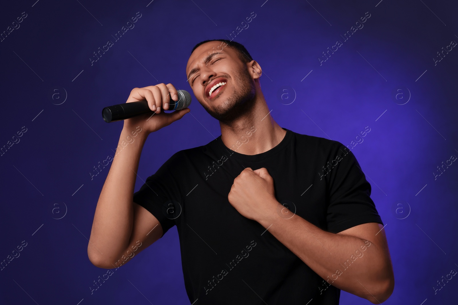 Photo of Handsome man with microphone singing on blue background