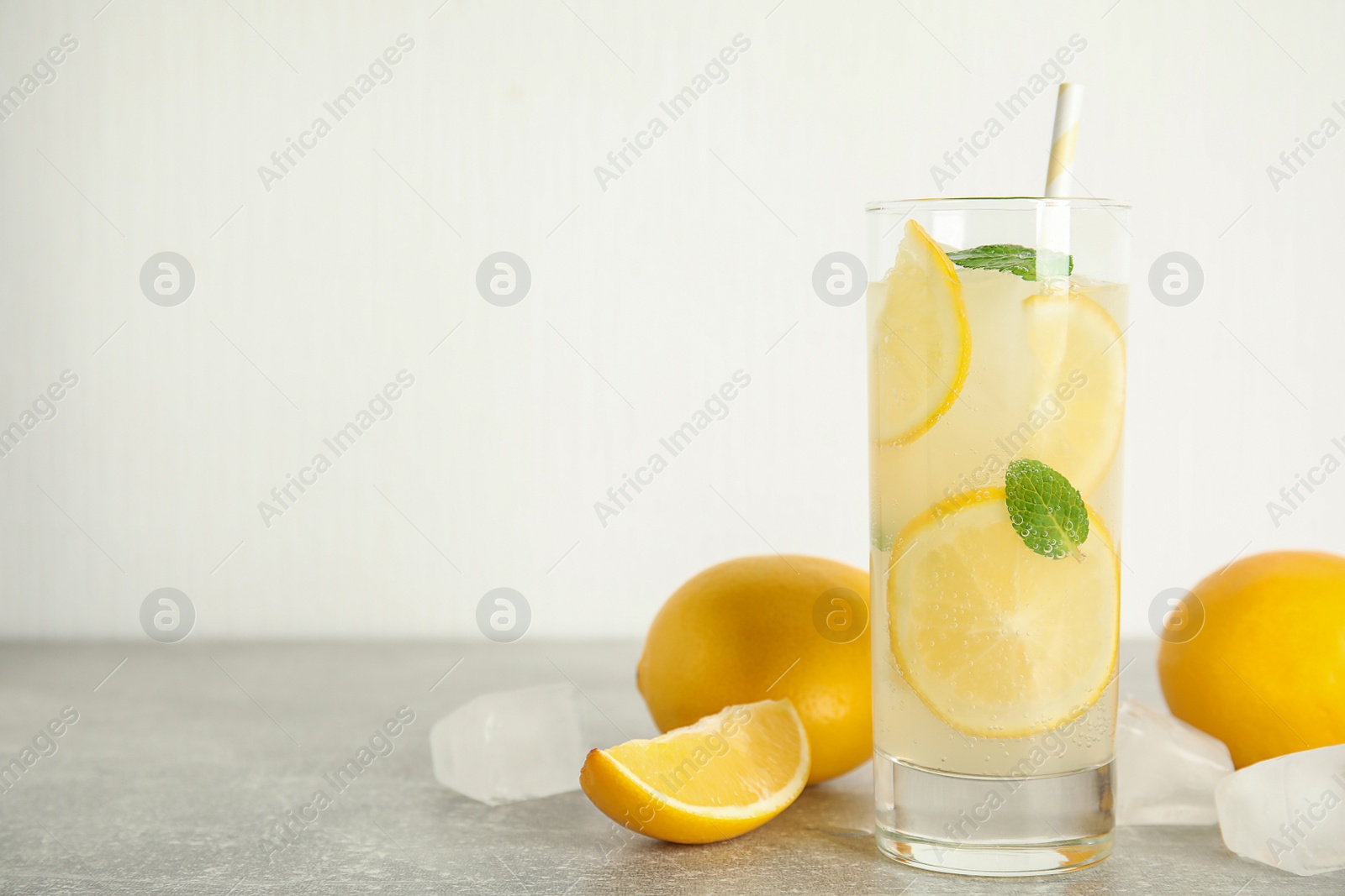 Photo of Cool freshly made lemonade, ice cubes and fruits on grey table. Space for text