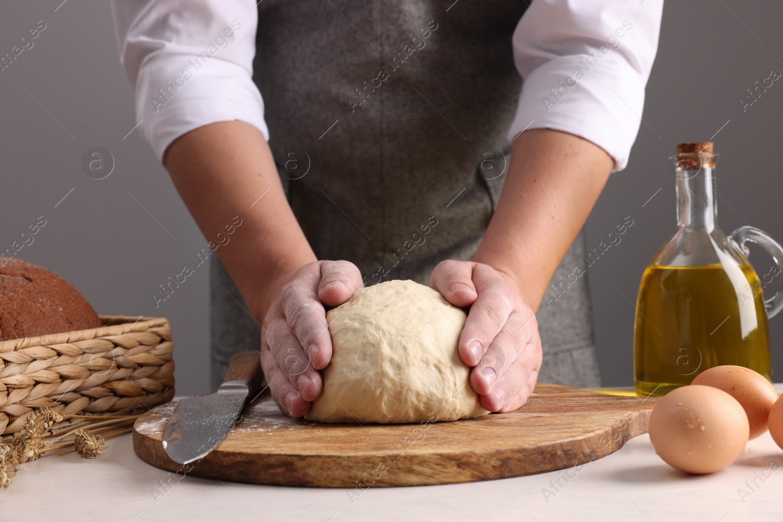 Photo of Man kneading dough at table near grey wall, closeup