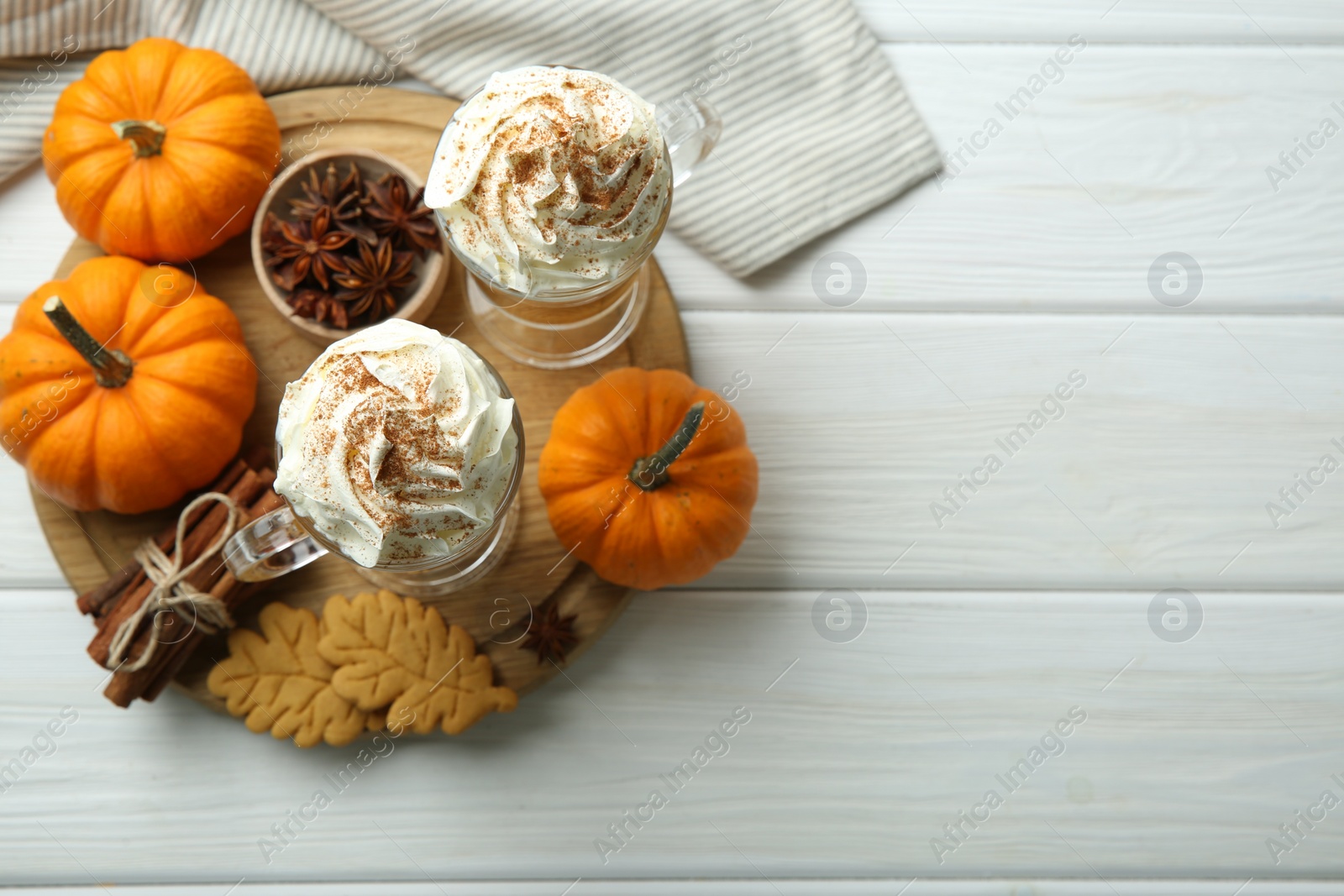 Photo of Tasty pumpkin latte with whipped cream in glasses, spices and cookies on white wooden table, top view. Space for text