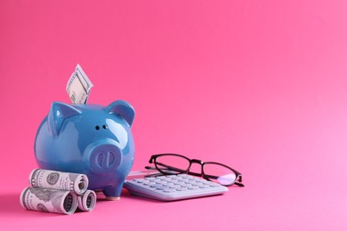 Photo of Financial savings. Piggy bank, dollar banknotes, glasses and calculator on pink background, space for text