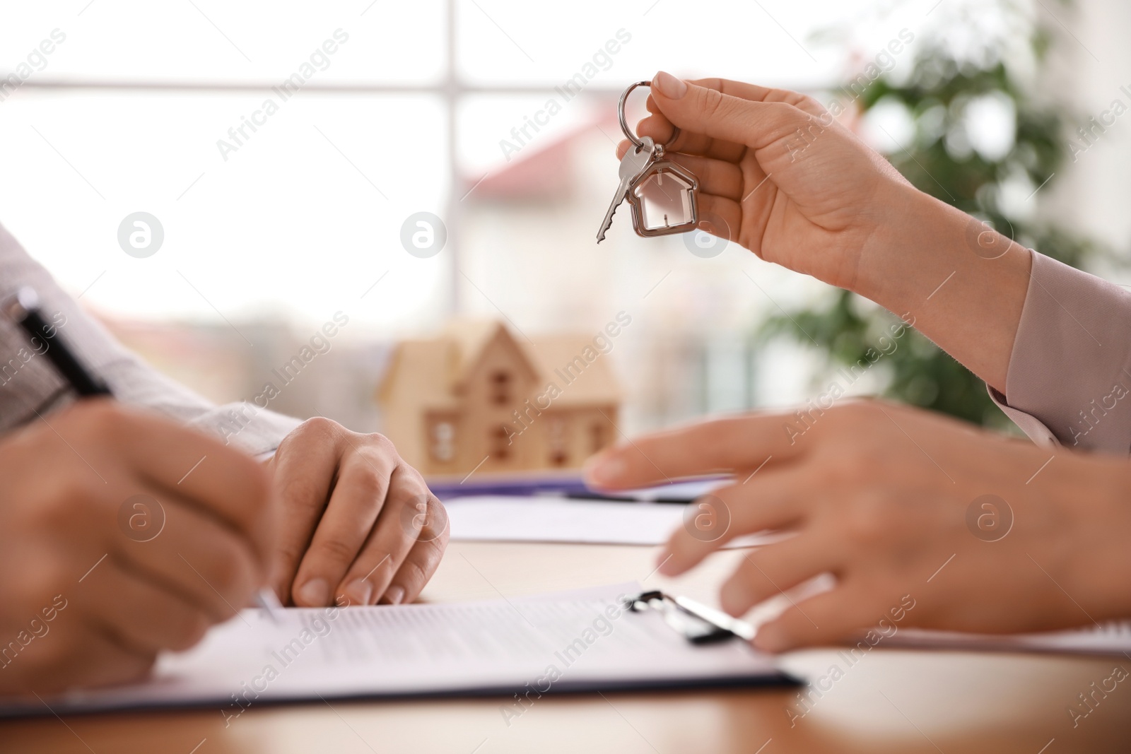 Photo of Real estate agent giving key with trinket to client in office, closeup