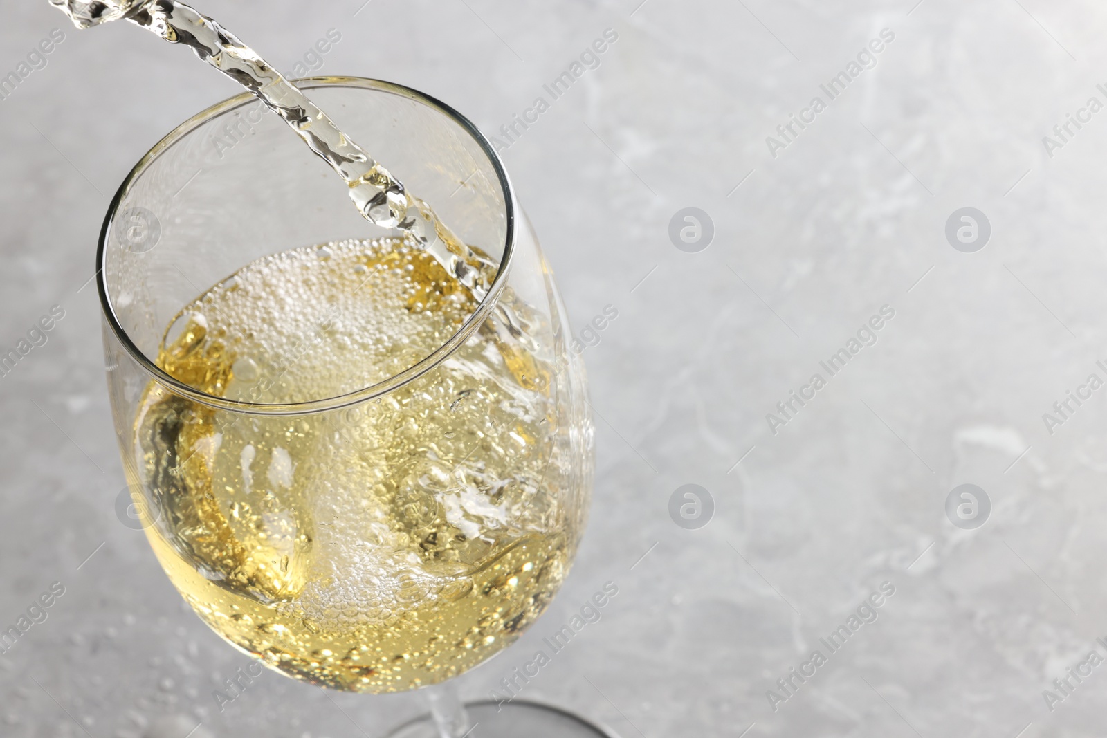 Photo of Pouring tasty aromatic wine in glass at gray marble table, closeup. Space for text