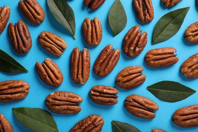 Photo of Flat lay composition with tasty pecan nuts and green leaves on light blue background