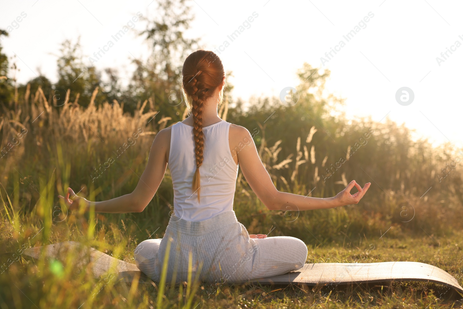 Photo of Woman practicing Padmasana on yoga mat outdoors on sunny day, back view. Lotus pose