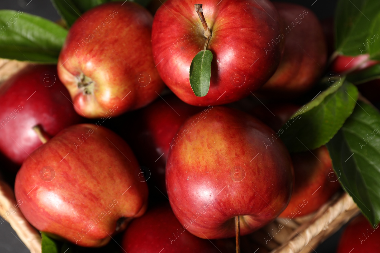 Photo of Fresh red apples with leaves in basket, closeup