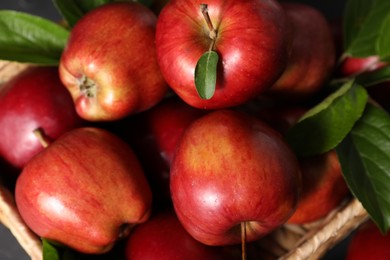 Photo of Fresh red apples with leaves in basket, closeup