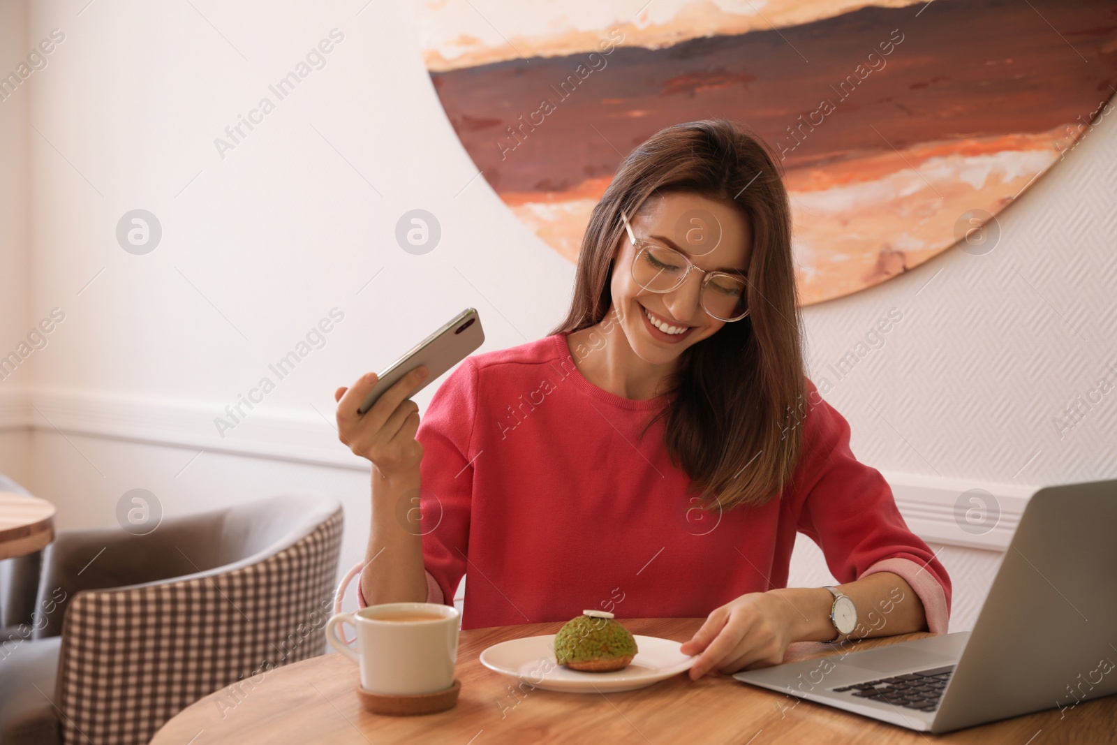 Photo of Young blogger taking photo of dessert at table in cafe