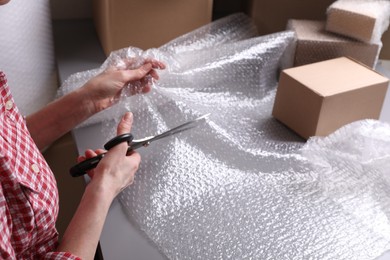 Photo of Woman cutting bubble wrap at table in warehouse, closeup