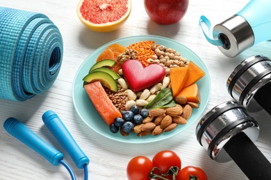 Photo of Plate with heart-healthy products and sports equipment on wooden background
