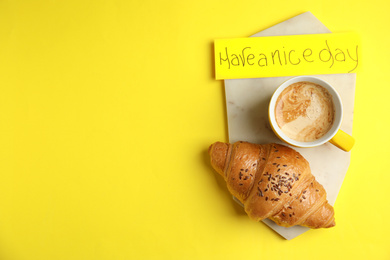 Photo of Delicious morning coffee, croissant and card with HAVE A NICE DAY wish on yellow background, flat lay. Space for text
